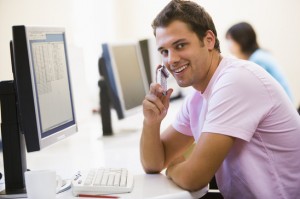 Man sitting in computer room using cellular phone and smiling